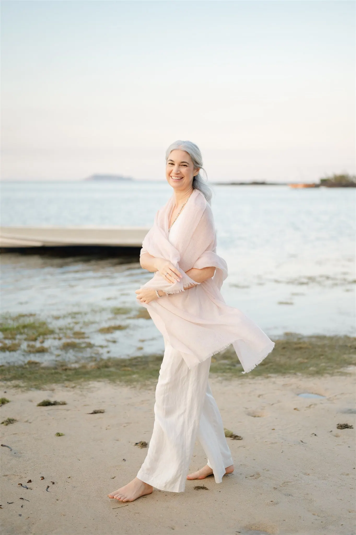Stephanie laughing on a beach at dusk, wrapped in a pale pink shawl
