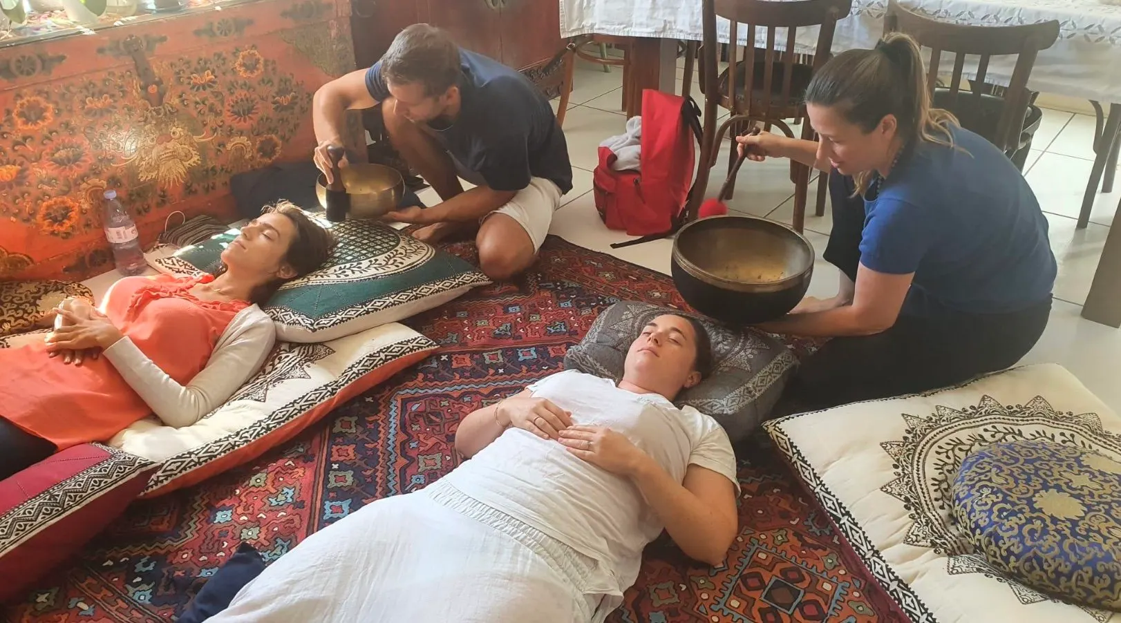 Two people lying on cushions during a breathwork and sound session, with singing bowls