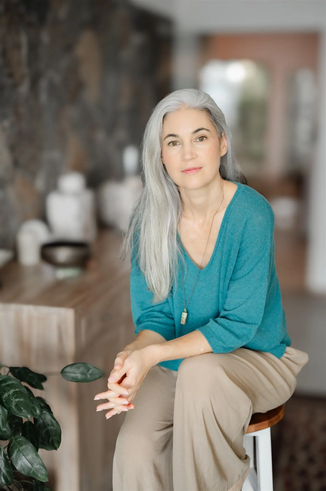 Stephanie Maurel seated in her practice room in a teal jumper, hands folded, against a stone wall