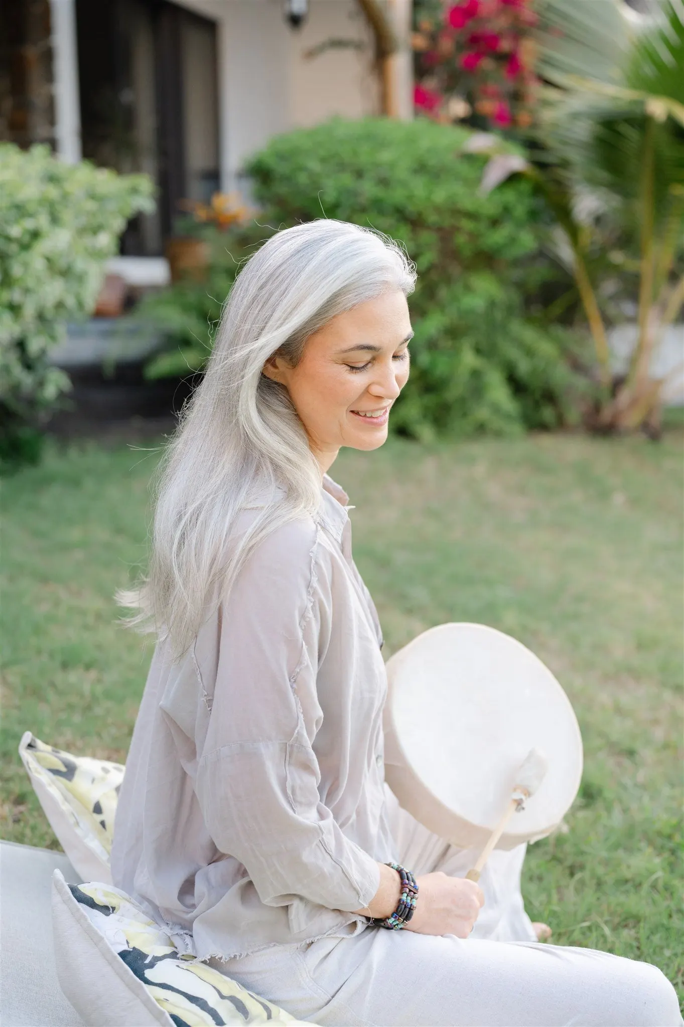 Stephanie seated in the garden, smiling, holding a frame drum